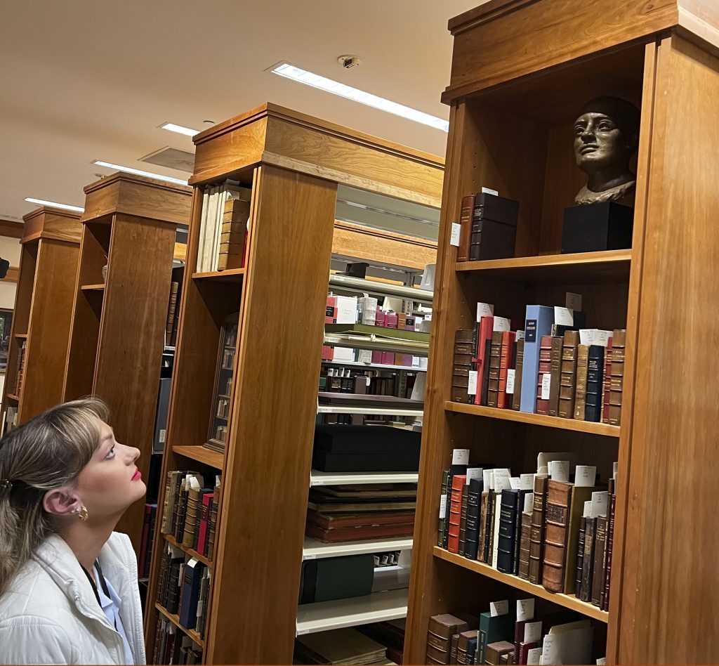 Christina is looking up at a bust housed in the vault with three books of shelves under it.