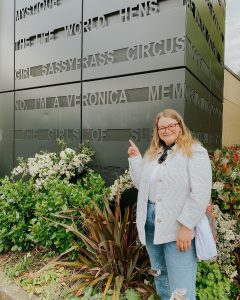 Photo of Veronica in a white coat pointing to a building sign which reads, "No, I'm a Veronica"