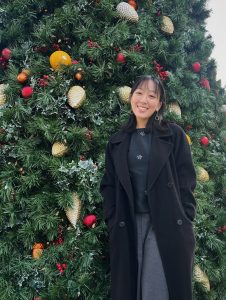 A photo of Jacquelyn standing outdoors in front of a Christmas tree.