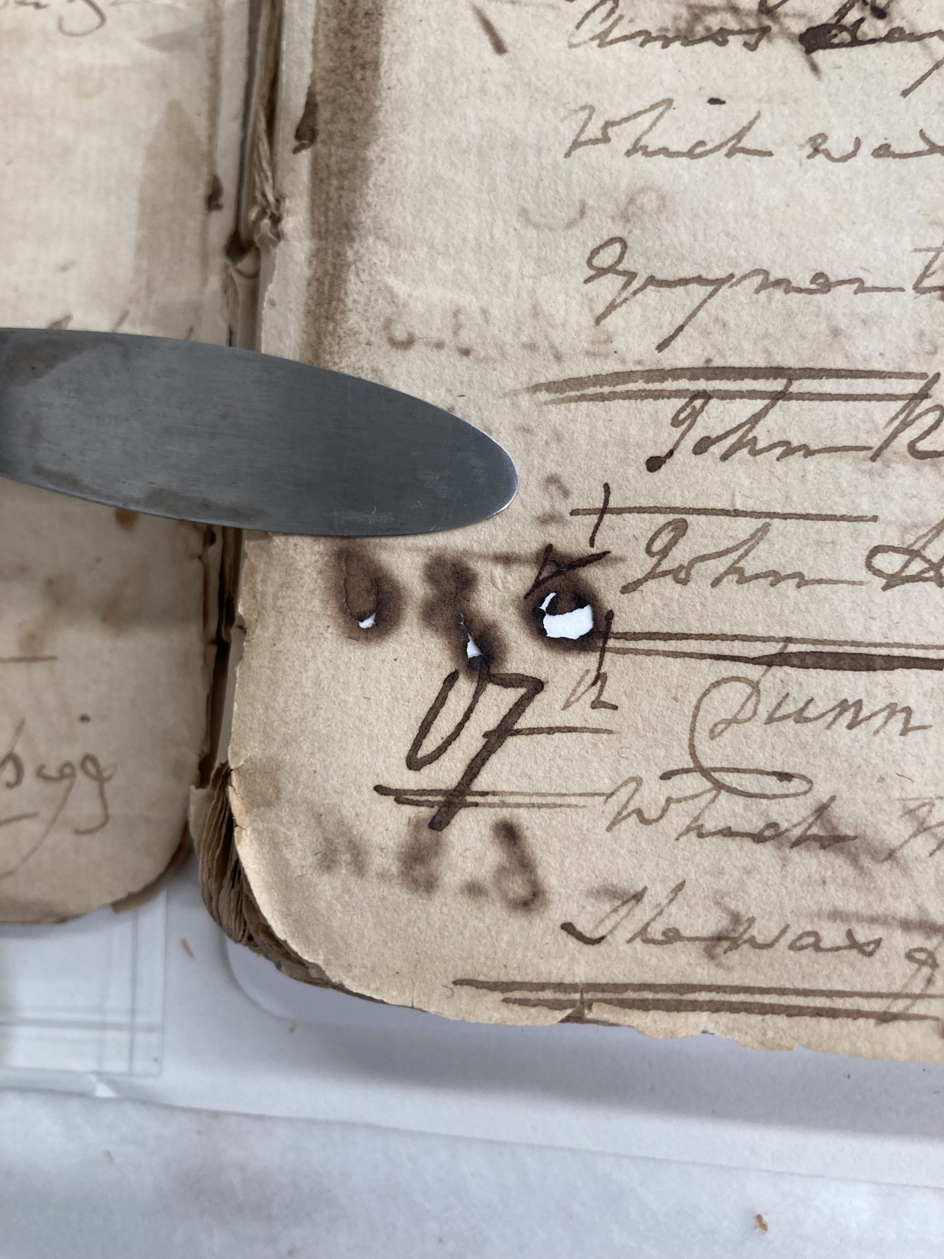 A beige sheet of paper with brownish-black ink that has a hole in it, made visible by a white background under the beige paper.